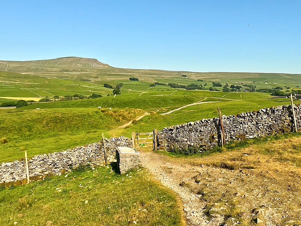 The path heads down to the information board by the gate in the wall