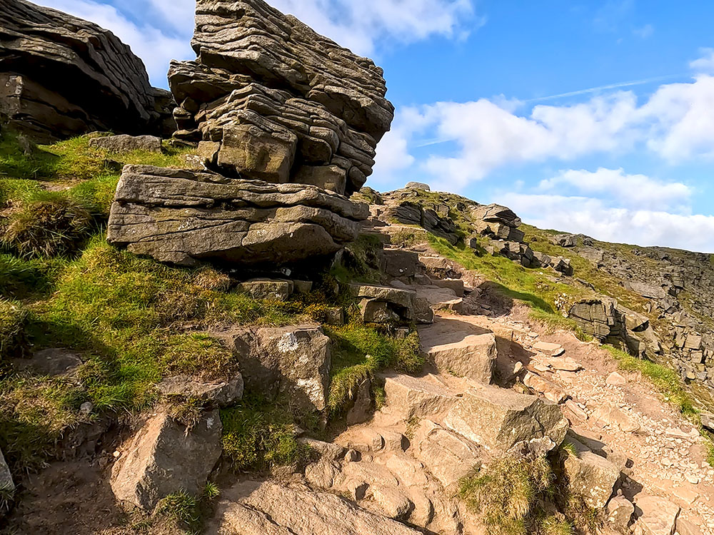 The path passes by the right-hand side of the large boulder